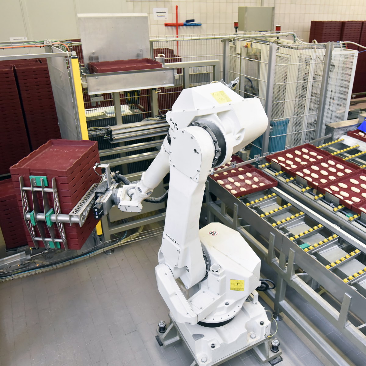 Robotic arm in a factory setting with conveyor belts and storage racks.